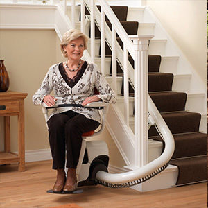 an affluent woman is sat at the bottom of her stairs on a curved rail stairlift.
