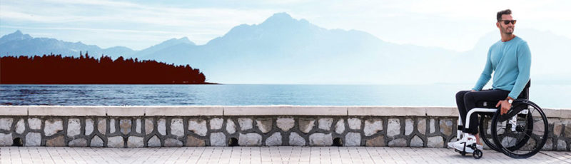 A man sits on a path next to a beautiful lake. The atmosphere above is hazy but sunny.